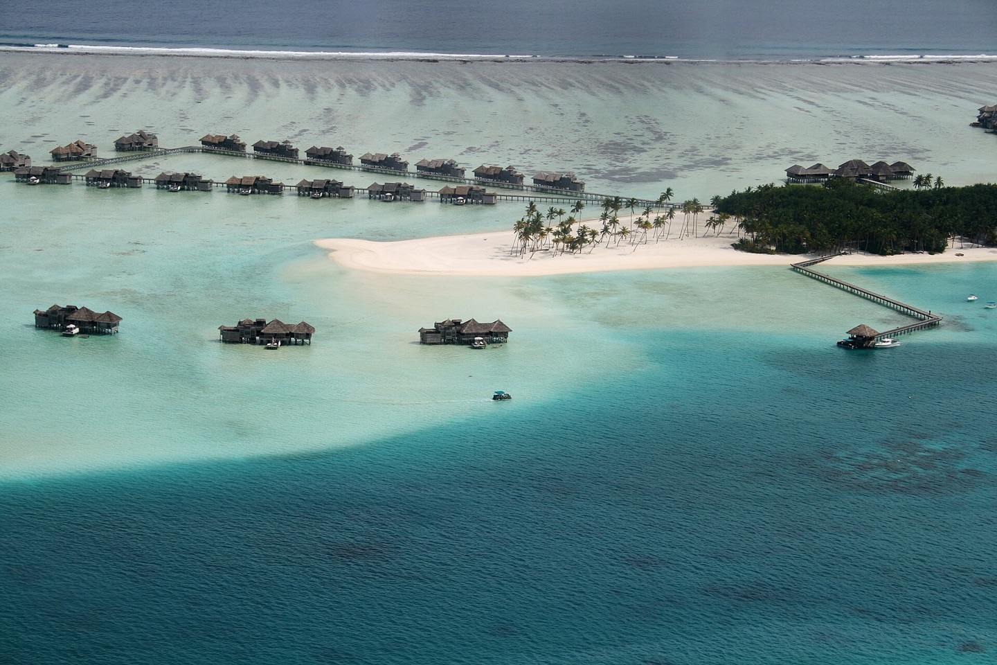 Aerial view of a green Maldives island surrounded by turquoise reef and ocean